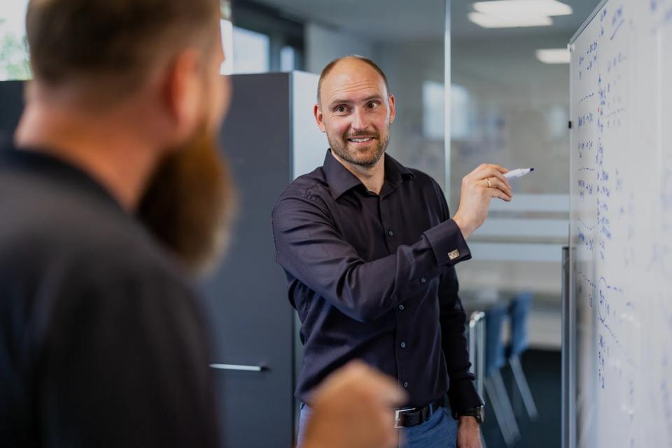 Mand skriver på tavle og korresponderer med kollega