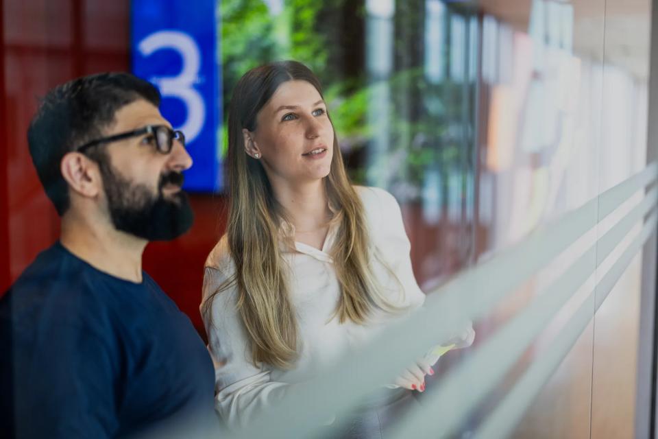 To kollegaer, der kigger på post it notes på en glasvæg